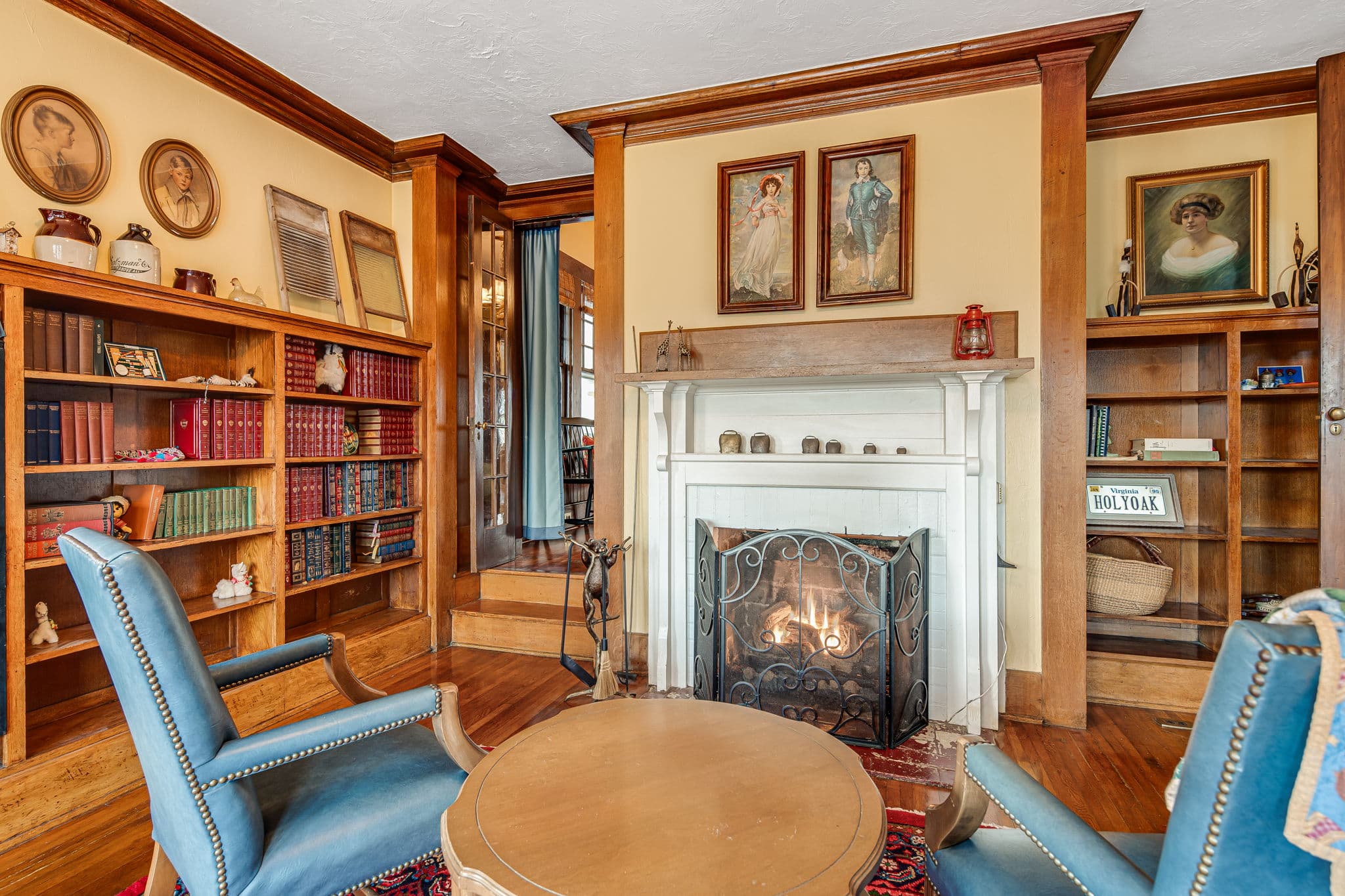 Library, international decorations, blue leather chairs, side table, fireplace, books, entrance to foyer