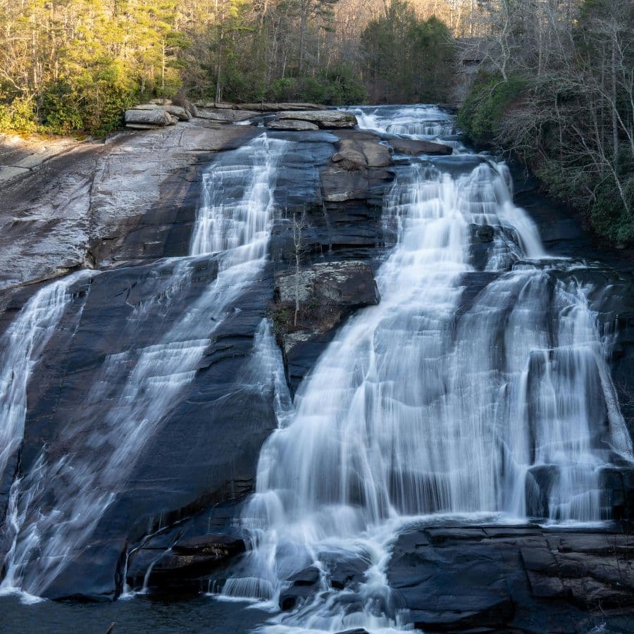 A cascading waterfall flows over dark rocks surrounded by lush trees.