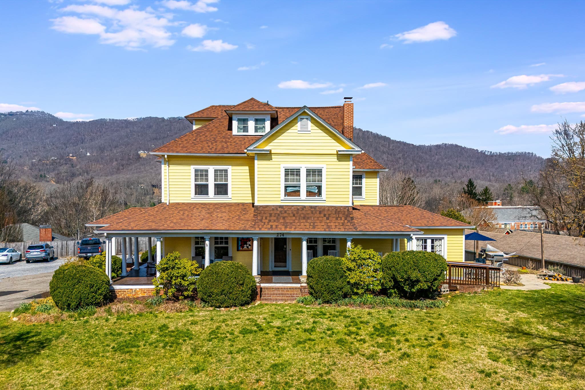yellow historic inn with brown roof, bushes, grass, mountains in background, blue skies
