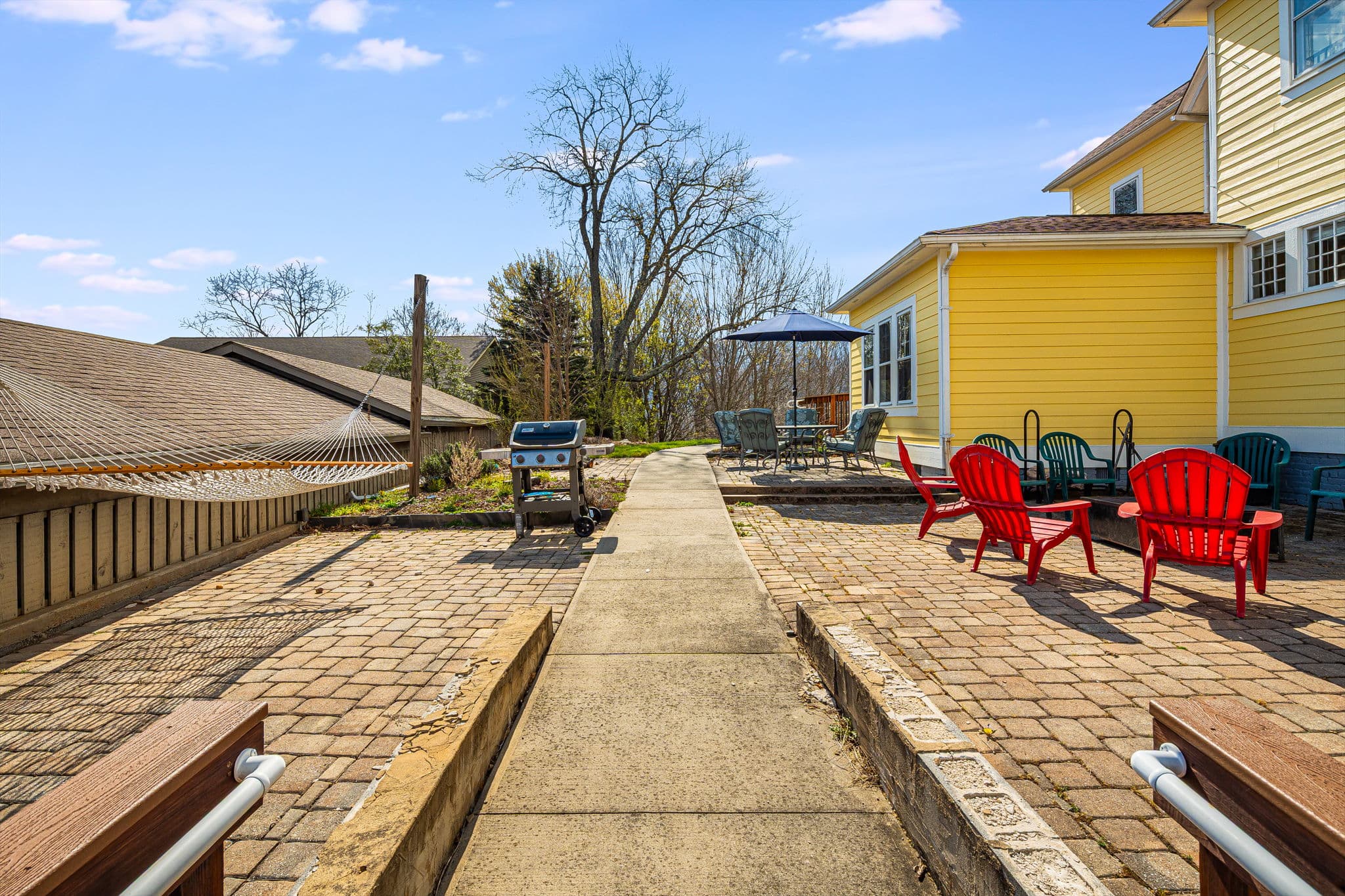 outside patio with handicap ramp, red Adirondack chairs, fire pit, blue skies, trees, bricks