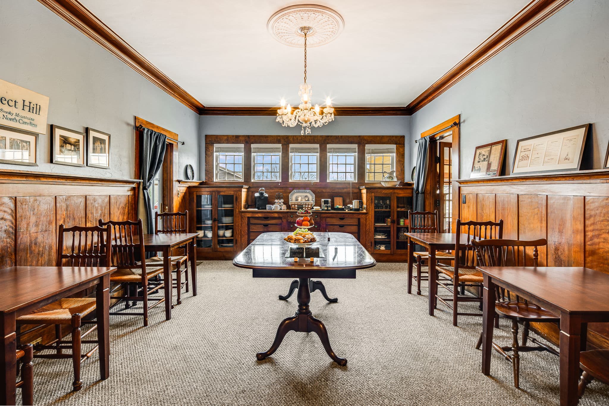 dining room with five tables and eight chairs, five windows, historic photos and memorabilia on wall, crystal chandelier