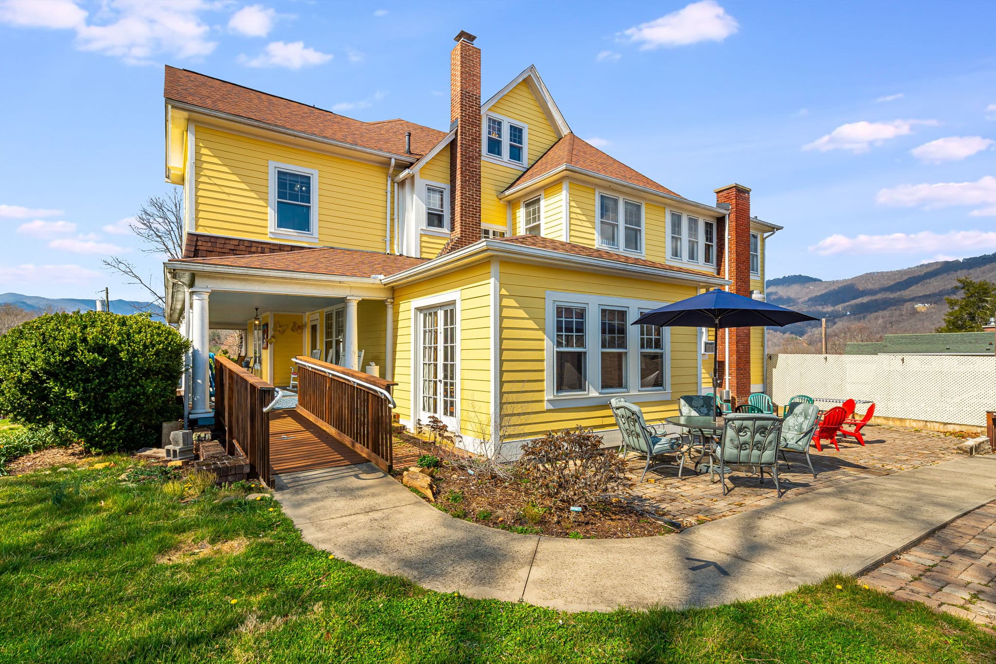 large historic yellow house or inn, outside patio, red Adirondack chairs, fire pit, blue skies, mountain views, bricks, white privacy fence, handicap accessible ramp