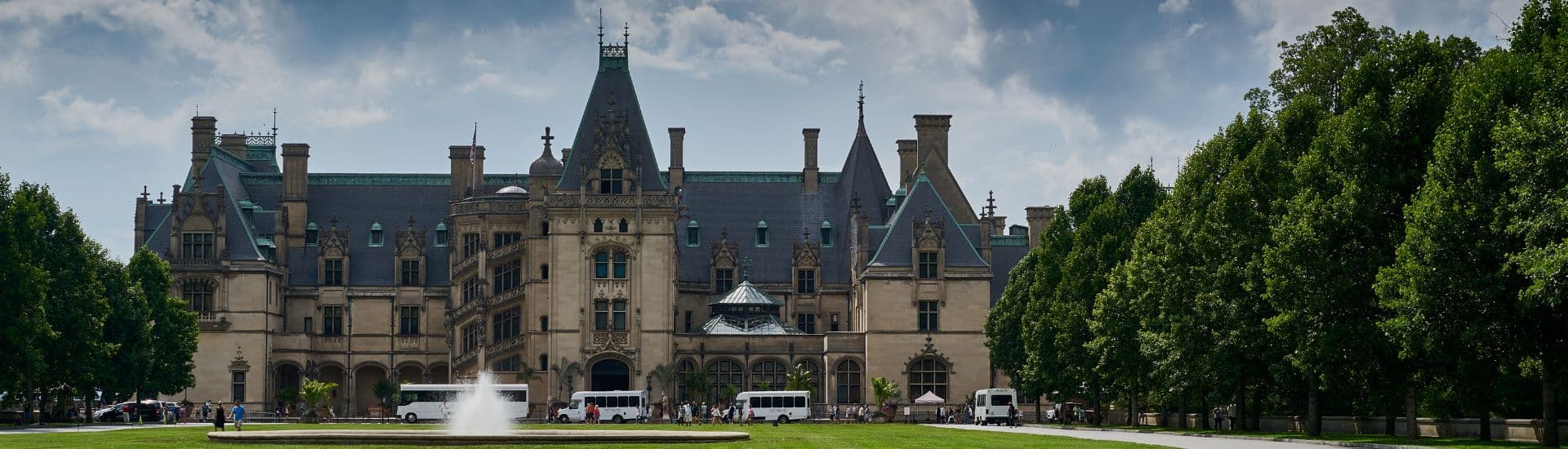 A grand mansion surrounded by lush greenery under a cloudy sky.
