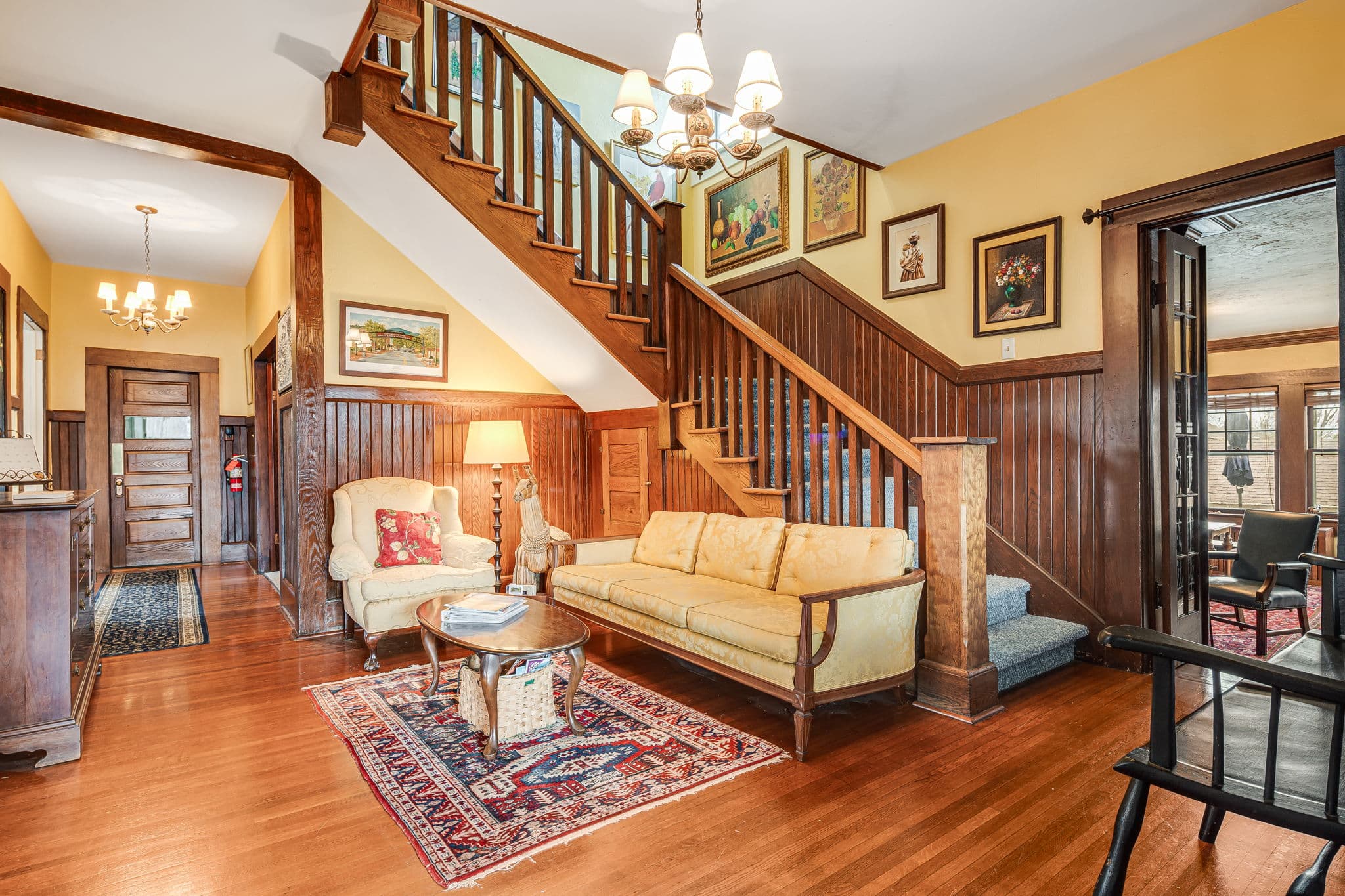 foyer, entrance, black bench, yellow sofa, yellow chair, oriental carpets, hallway, paintings, staircase with dark wood, doorway to library