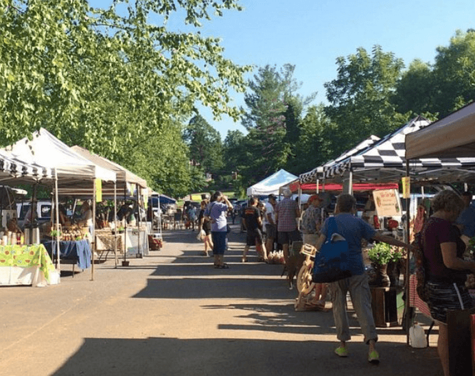 A bustling outdoor market with colorful tents and shoppers browsing various products under a clear blue sky.