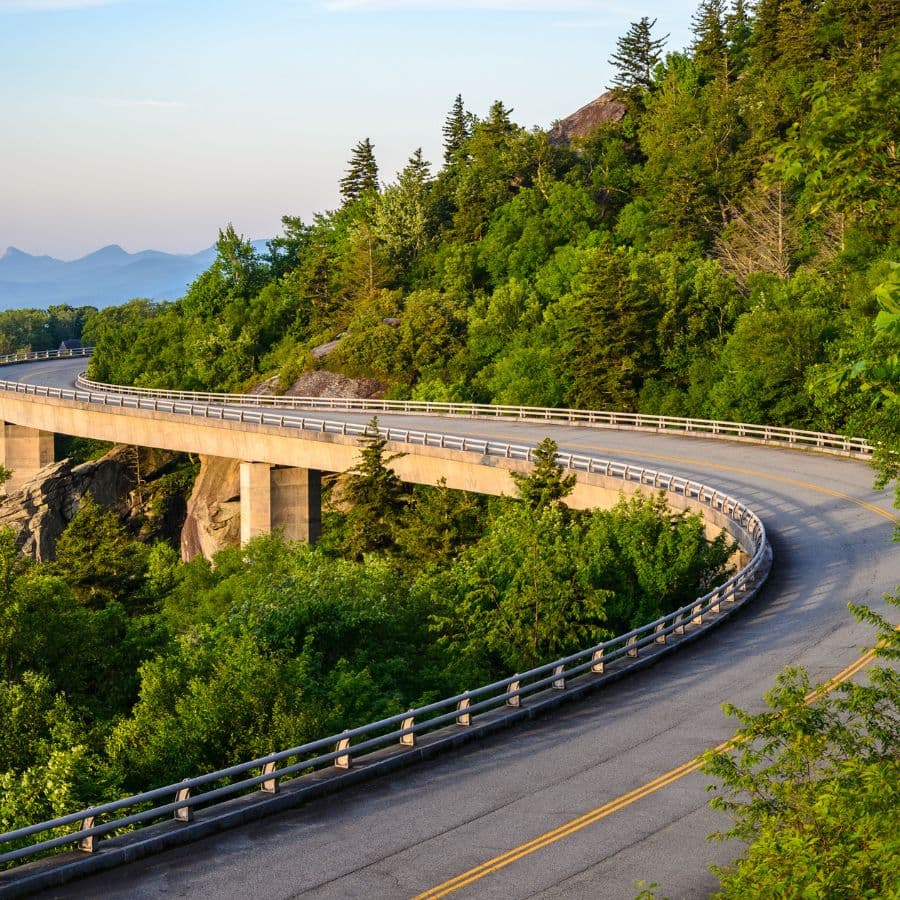A winding road curves gracefully through lush greenery with mountains in the distance.