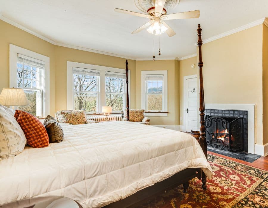 Cozy bedroom with a four-poster bed, fireplace, and large windows offering scenic views.