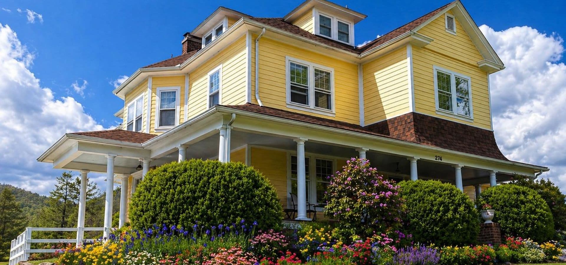 A charming yellow house surrounded by vibrant flower gardens under a blue sky.
