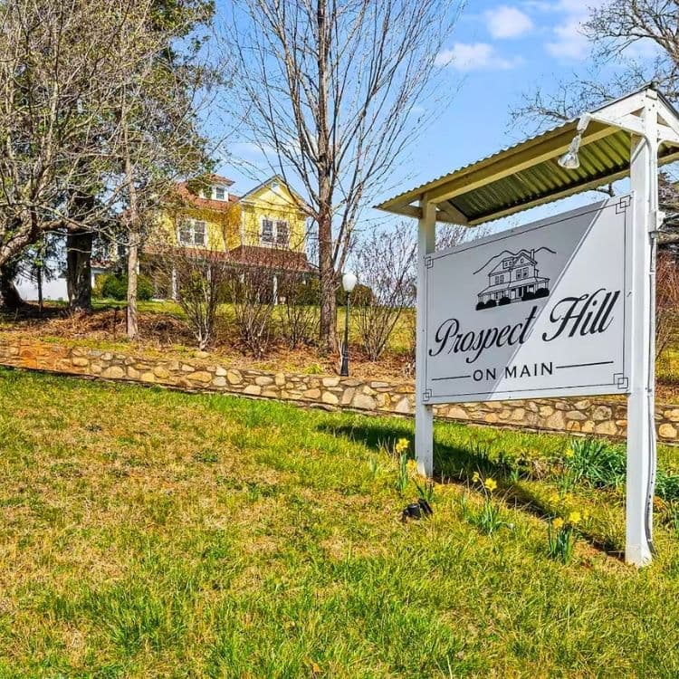 Sign for Prospect Hill on Main with a yellow house in the background.