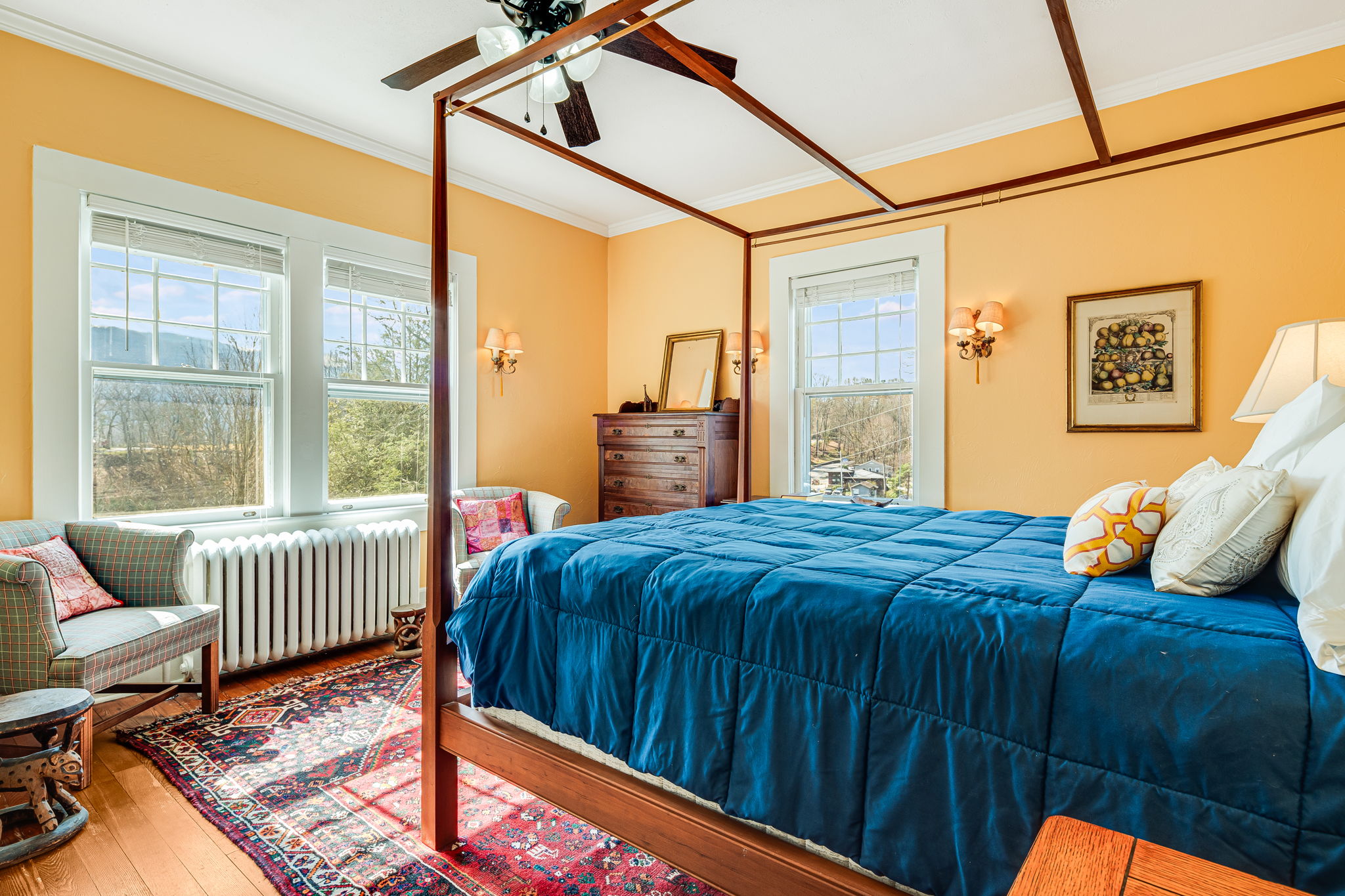 queen bed with blue bedspread, windows, chair, dresser